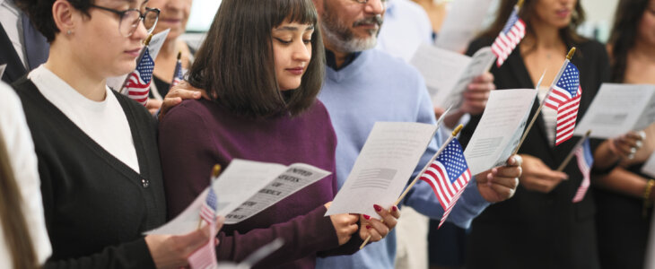 A diverse group of people in a ceremony taking the United States Naturalization Oath of Allegiance to become citizens.