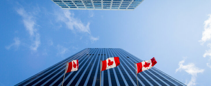 Picture of the canadian flag taken in front of a cold and blue business building in the CDB of Ottaawa. Ottawa is the capital city of Canada, and a major hub for economy, politics and business in America.