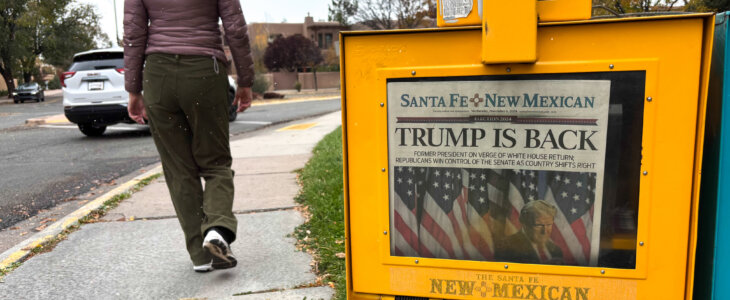 Santa Fe, NM: A woman walks past a Santa Fe New Mexican vending box in downtown Santa Fe, where the headline reads “Trump is Back.”